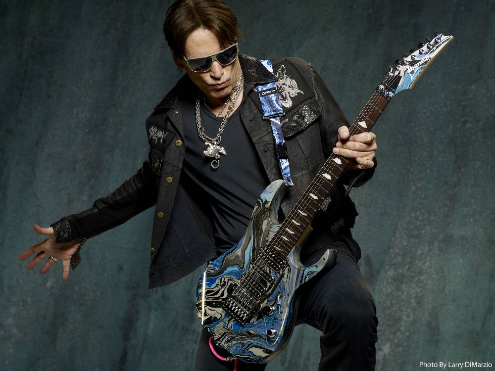 Steve Vai posing with his signature Ibanez Universe guitar, a symbol of his unique style and musical prowess.